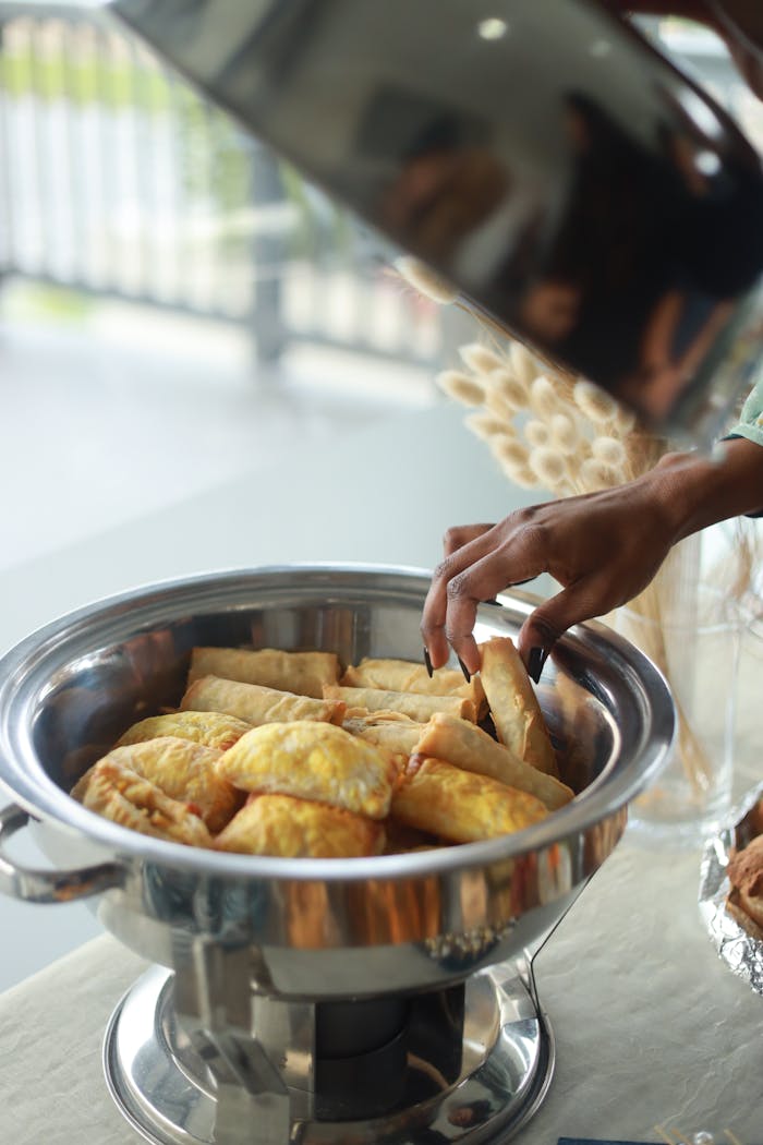 A hand reaching for delicious pastries in a chafing dish at a buffet. Perfect for food lifestyle content.