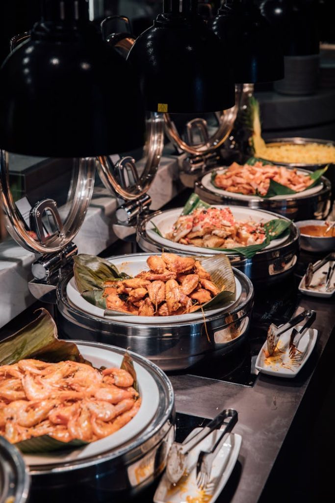 Assorted buffet dishes under warm lights, featuring chicken wings, vegetables, and more.