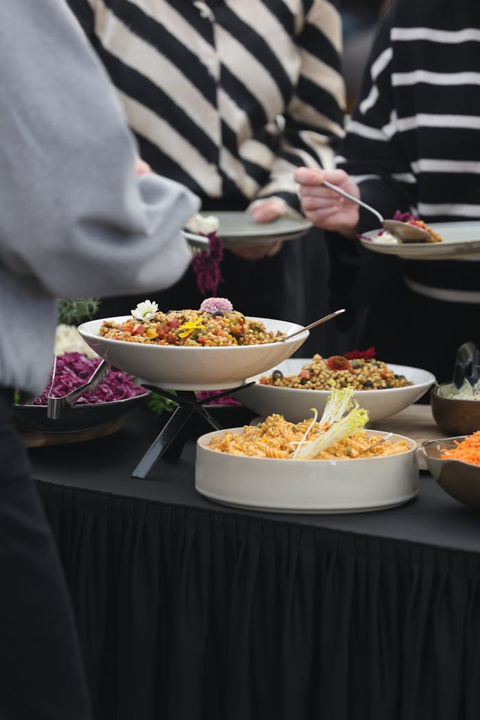 A diverse array of colorful dishes on a buffet table at a gathering, featuring salads and grains.
